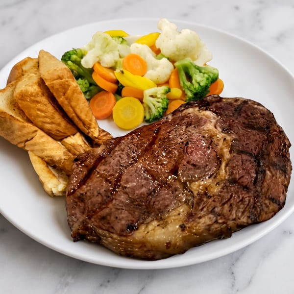 Grilled steak with grill marks, a side of golden fries, and mixed steamed vegetables on a white plate.