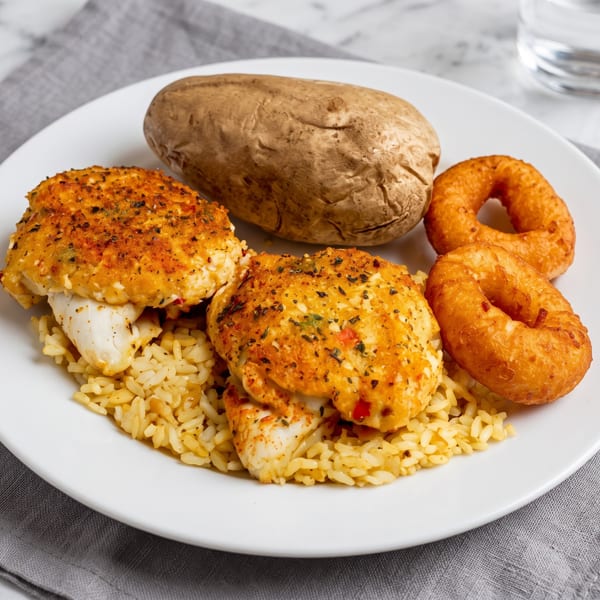 A plate of baked fish, rice, a baked potato, and two onion rings.