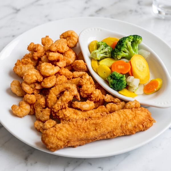 Fried shrimp and fish with a side of steamed broccoli, carrots, and squash on a white plate.